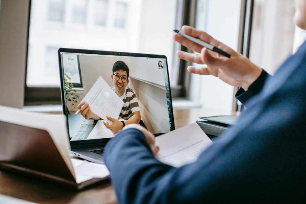 A picture of a video call on a laptop, there is a smiling man on the laptop screen speaking to the user who is off screen